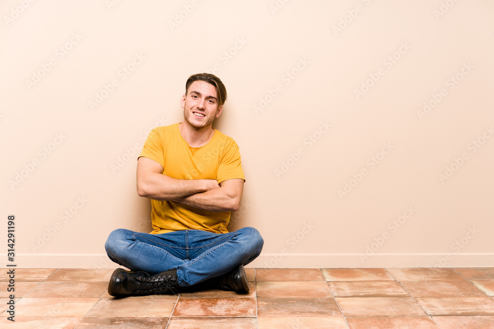 Young caucasian man sitting on the floor isolated laughing and having fun.