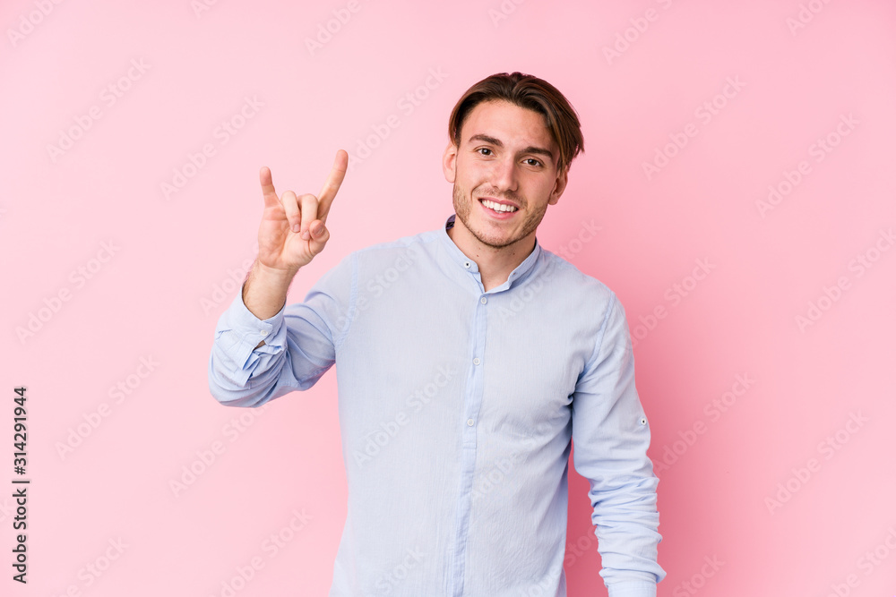 Young caucasian man posing in a pink background isolated showing a horns gesture as a revolution concept. Young caucasian man posing in a pink background isolated showing a horns gesture as a revolution concept.