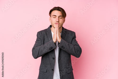Young caucasian business man posing isolated holding hands in pray near mouth, feels confident.