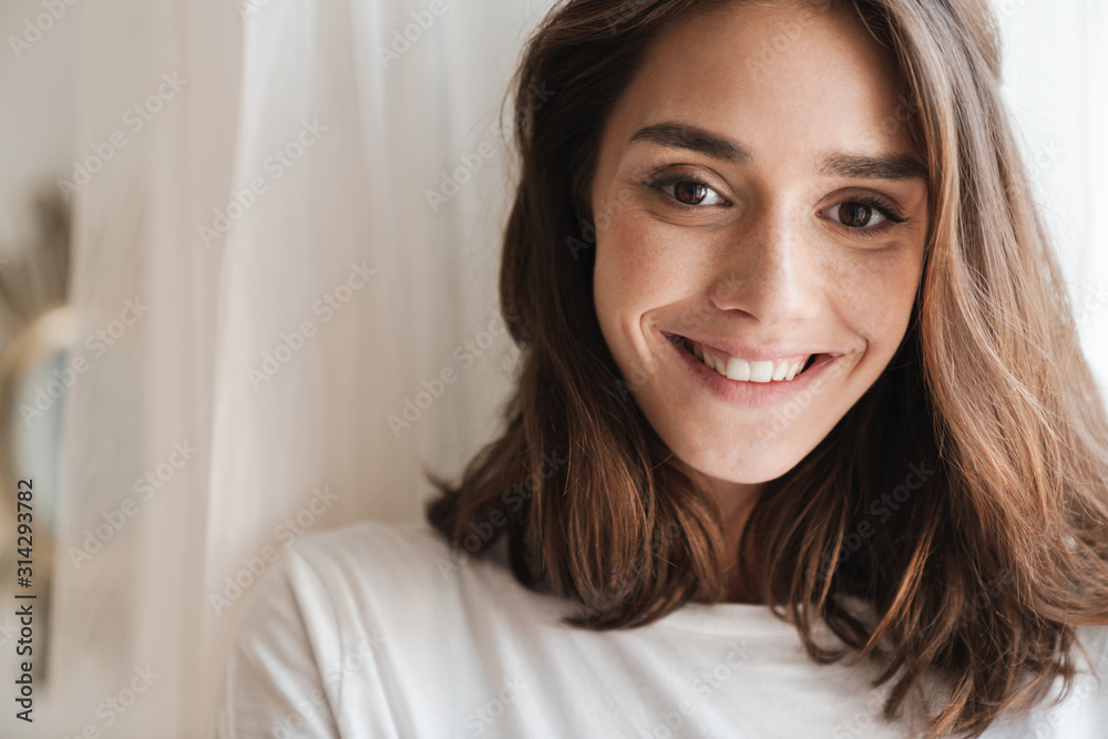 Cheery young woman indoors at home posing near window. Cheery young woman indoors at home posing near window.