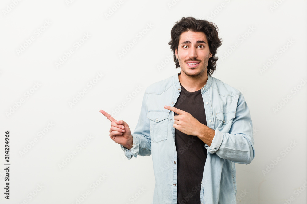 Young handsome man against a white background shocked pointing with index fingers to a copy space. Young handsome man against a white background shocked pointing with index fingers to a copy space.