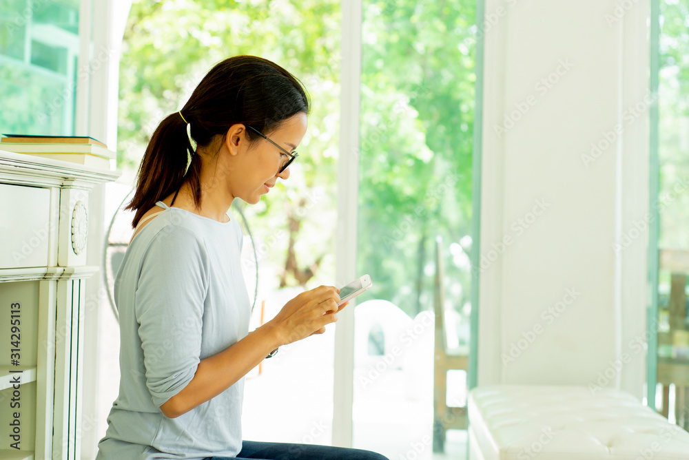 Happy Asian woman sitting on sofa at living room using smartphone Happy Asian woman sitting on sofa at living room using smartphone
