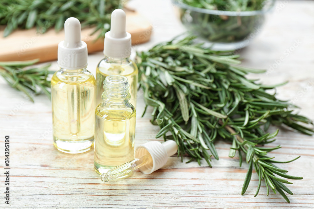 Bottles of rosemary essential oil on white wooden table Bottles of rosemary essential oil on white wooden table
