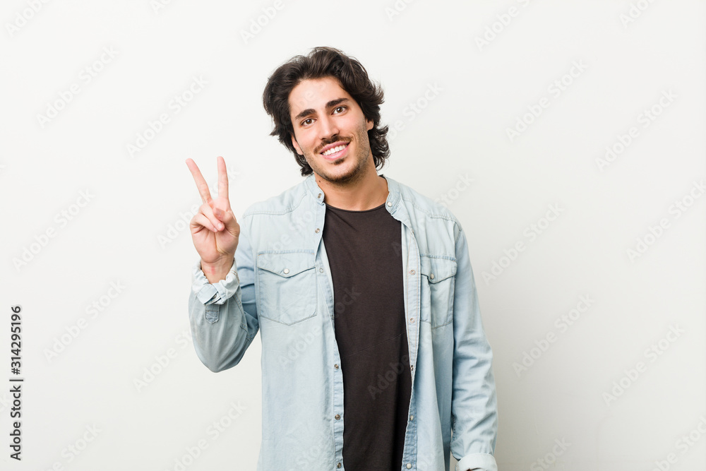 Young handsome man against a white background joyful and carefree showing a peace symbol with fingers. Young handsome man against a white background joyful and carefree showing a peace symbol with fingers.