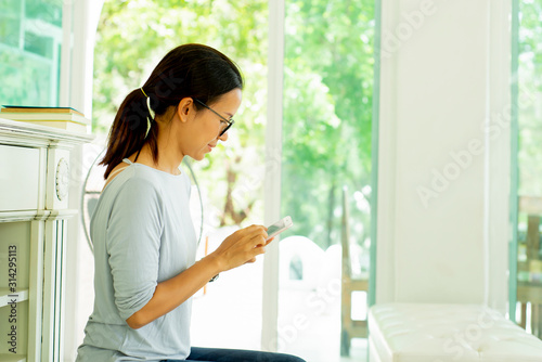 Happy Asian woman sitting on sofa at living room using smartphone
