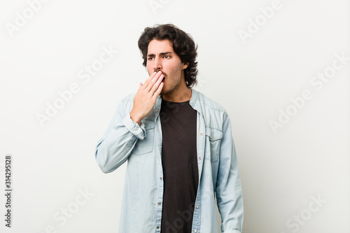 Young handsome man against a white background yawning showing a tired gesture covering mouth with hand.