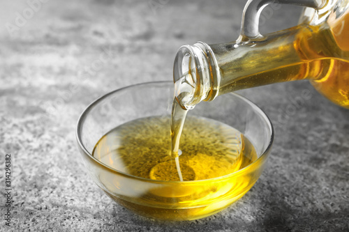 Pouring cooking oil from jug into bowl on grey table photo