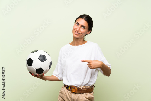 Young woman over isolated green background holding a soccer ball