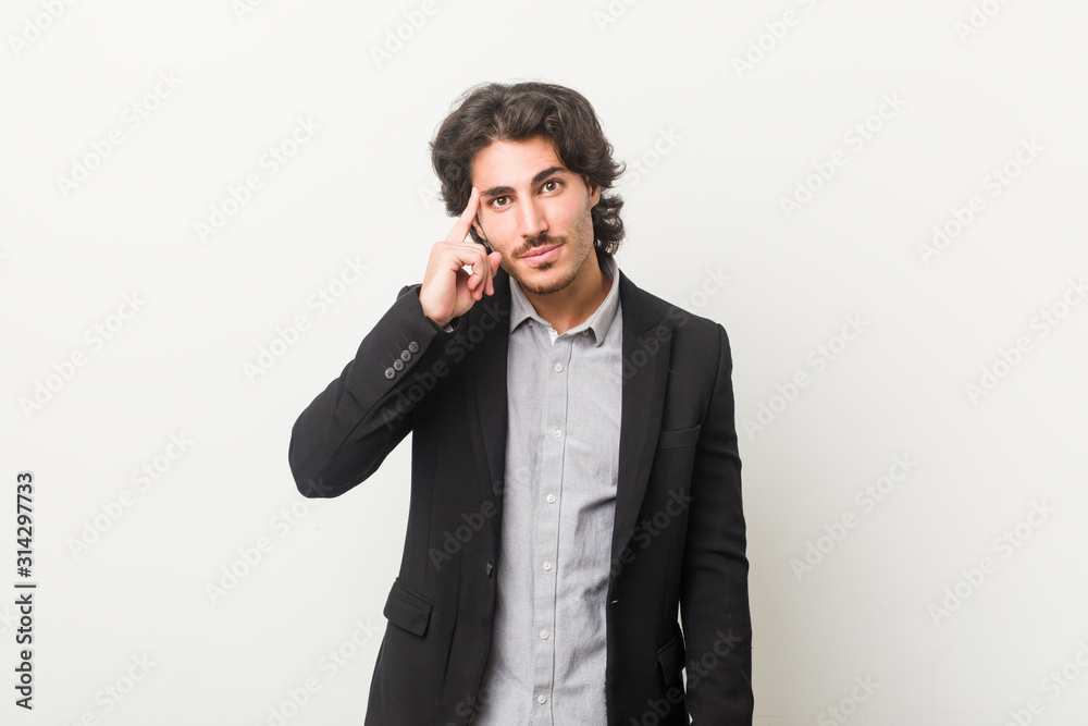 Young business man against a white background pointing temple with finger, thinking, focused on a task. Young business man against a white background pointing temple with finger, thinking, focused on a task.