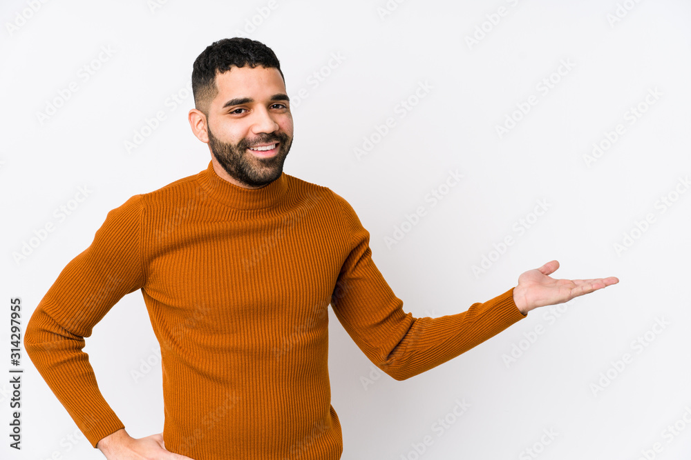 Young latin man against a white background isolated showing a copy space on a palm and holding another hand on waist. Young latin man against a white background isolated showing a copy space on a palm and holding another hand on waist.