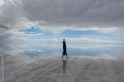 Woman in handstand in centre of view of Salar De Uyuni Saltflats, Bolivia, with water reflecting sky and mountains. photo