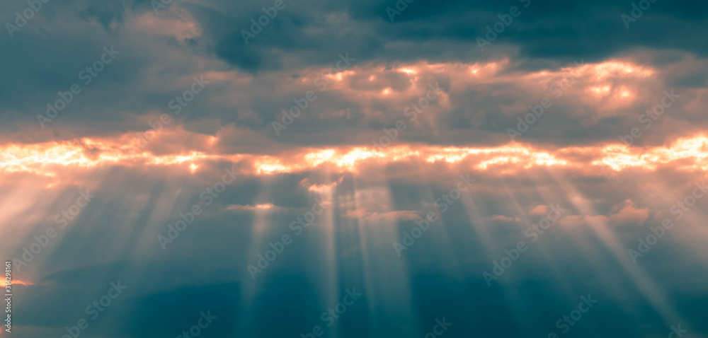 A background from a heavy dark thunderstorm sky with oblique rays of sun breaking through the clouds. State of the atmosphere before the storm