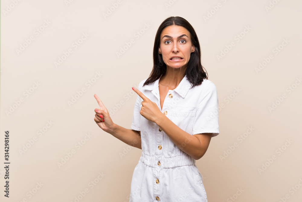 Young woman over isolated background frightened and pointing to the side