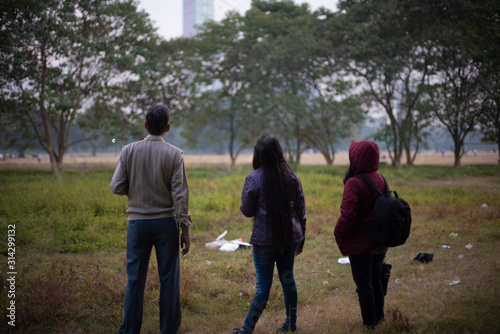 Back side of an Indian Bengali family in winter jacket and sweater enjoying an outing in a dry grass field in winter afternoon in natural background. Indian lifestyle and winter.