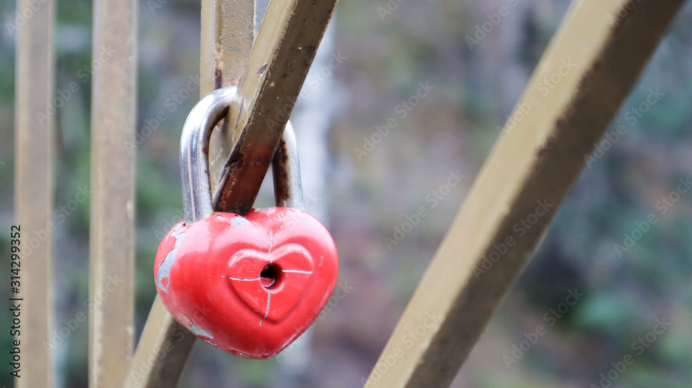 Shabby red lock in the shape of a heart. Valentine's day love concept. A padlock hanging on a metal railing is a sign of eternal love. The tradition of hooking a castle with a fence