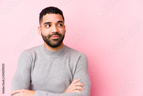 Young latin man against a pink background isolated smiling confident with crossed arms.