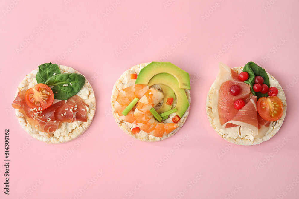 Puffed rice cakes with different toppings on pink background, flat lay