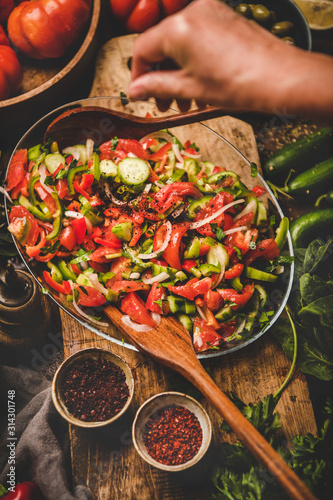 Flat-lay of womans hands adding spices to Turkish Chopard Salad made of fresh vegetables, herbs with olives, top view. Middle eastern, Mediterranean typical cuisine, vegan healthy dish