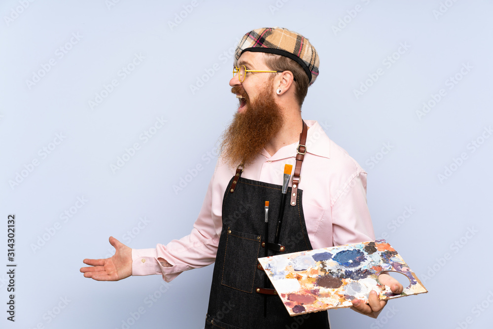 Redhead artist man with long beard holding a palette over isolated blue background with surprise facial expression Redhead artist man with long beard holding a palette over isolated blue background with surprise facial expression