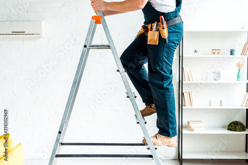 cropped view of installer in overalls climbing ladder