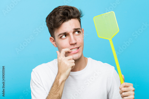 Young caucasian man holding a fly swatter relaxed thinking about something looking at a copy space. photo