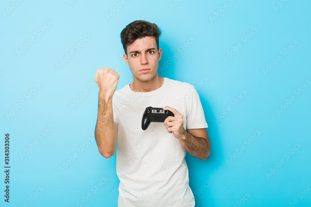 Young caucasian man playing videogames with game controller showing fist to camera, aggressive facial expression. Young caucasian man playing videogames with game controller showing fist to camera, aggressive facial expression.