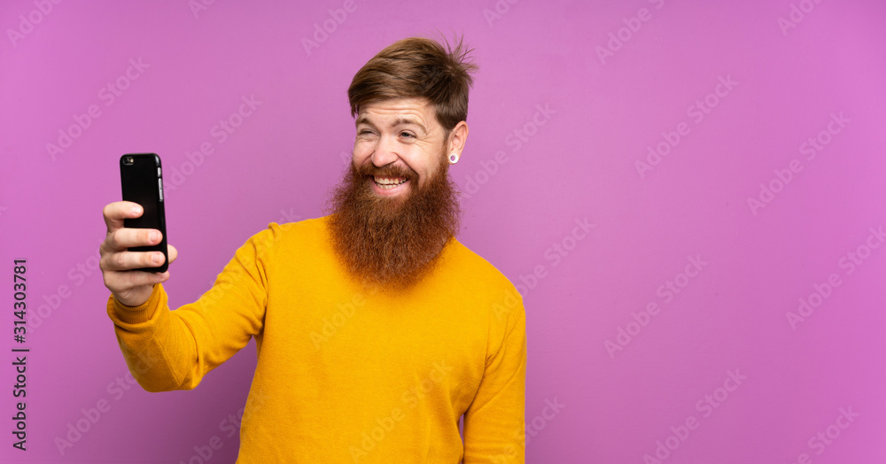 Redhead man with long beard over isolated purple background making a selfie Redhead man with long beard over isolated purple background making a selfie
