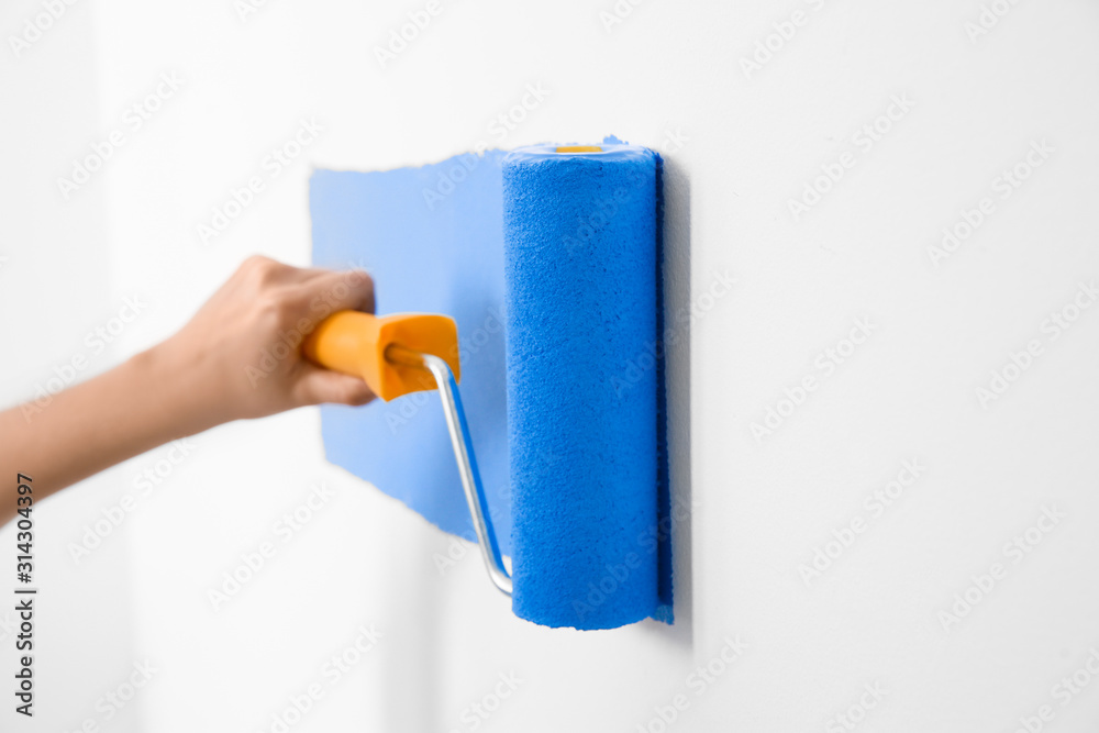 Obraz premium Woman painting white wall with blue dye, closeup. Interior renovation