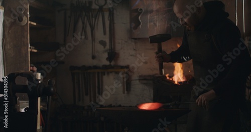 Blacksmith hammering heated iron on ironsmith and making a knife