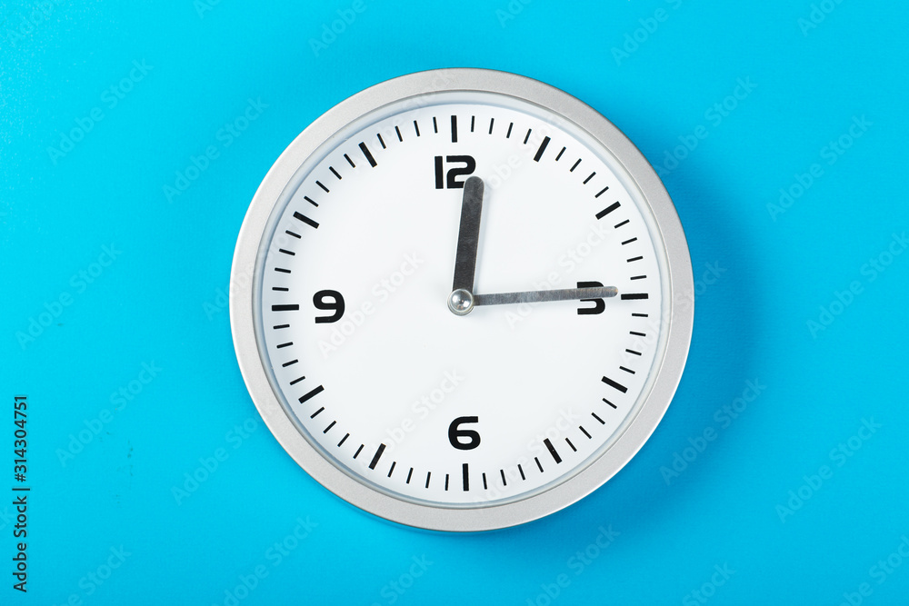 White wall clock with a yellow used hanging on the wall. Minimalist image of a wall clock on a blue background with copy space White wall clock with a yellow used hanging on the wall. Minimalist image of a wall clock on a blue background with copy space