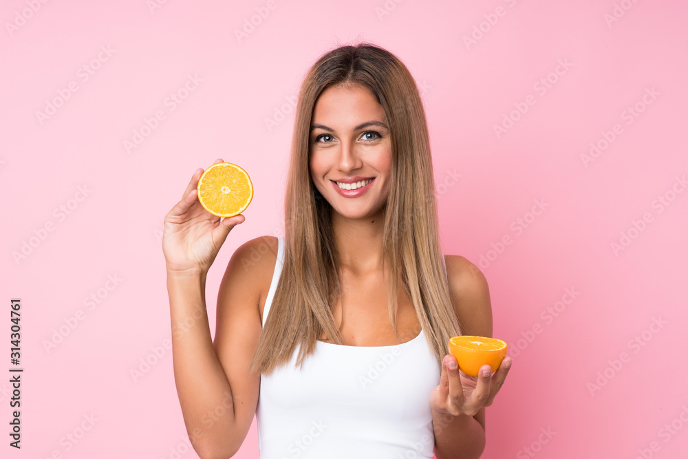Young blonde woman over isolated background holding an orange Young blonde woman over isolated background holding an orange