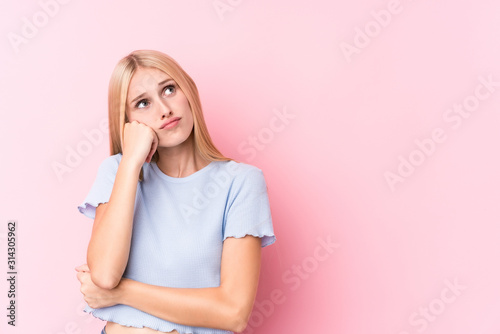 Young blonde woman on pink background who feels sad and pensive, looking at copy space.