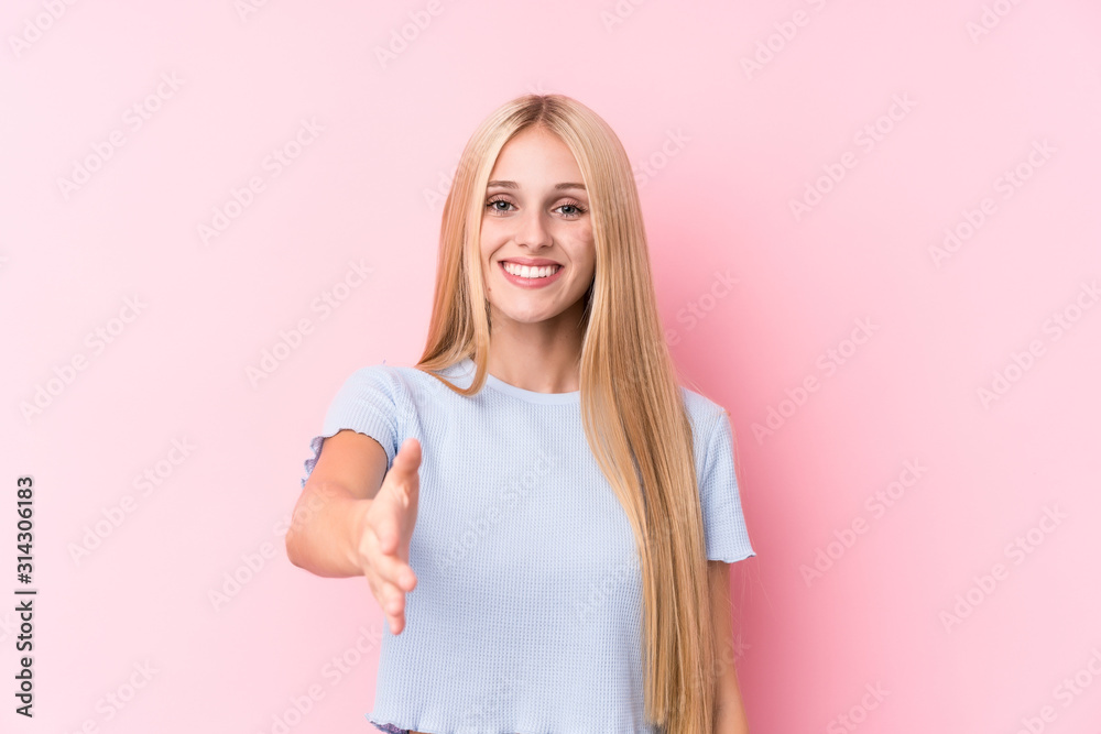 Young blonde woman on pink background stretching hand at camera in greeting gesture. Young blonde woman on pink background stretching hand at camera in greeting gesture.