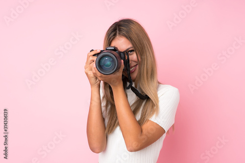 Young blonde woman over isolated pink background with a professional camera photo
