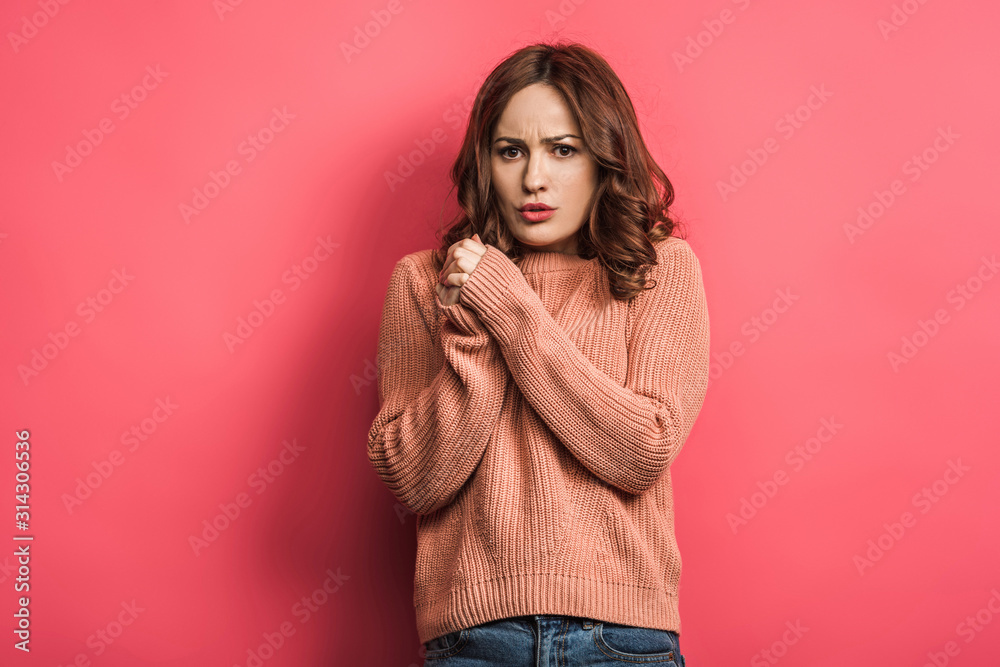 frozen girl standing with clenched hands and looking at camera on pink background frozen girl standing with clenched hands and looking at camera on pink background