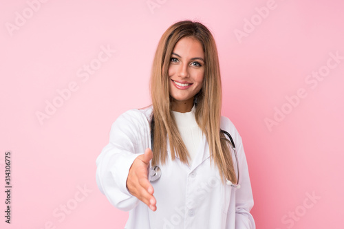 Young blonde woman over isolated pink background with doctor gown and making a deal