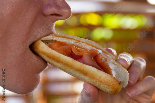 Close up on mouth of woman having a bite of salmon sandwich with mayonnaise. Restaurant  fast food lunch concept