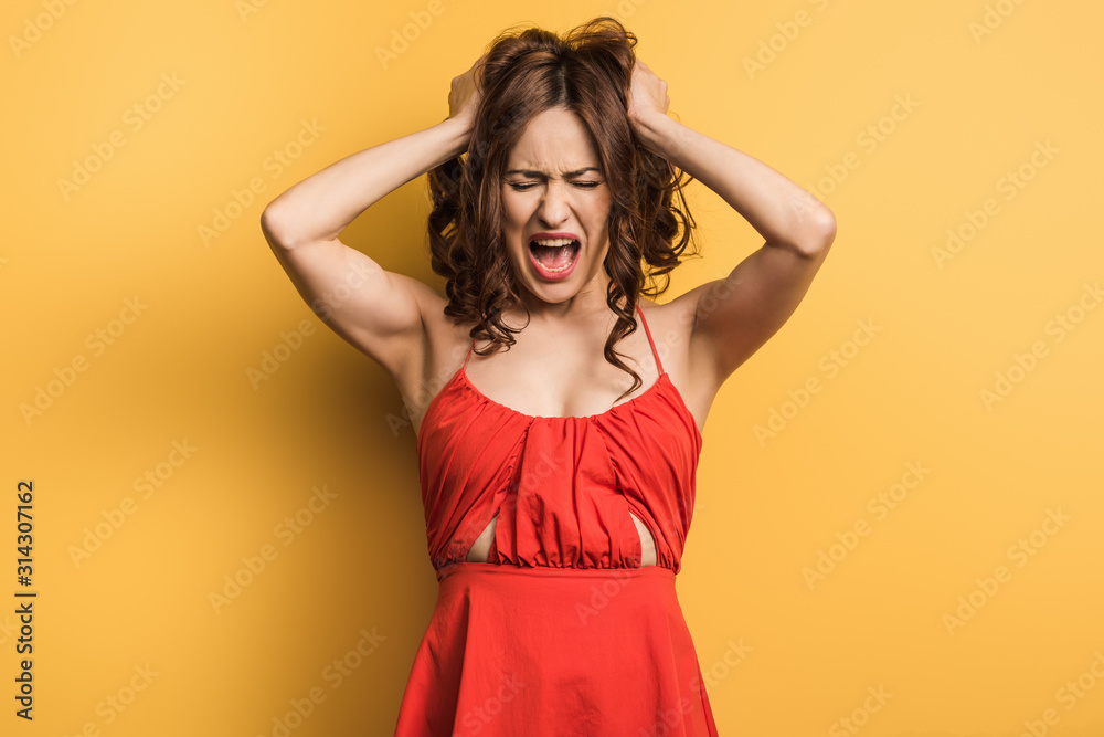 angry young woman screaming while standing with closed eyes and touching hair on yellow background angry young woman screaming while standing with closed eyes and touching hair on yellow background