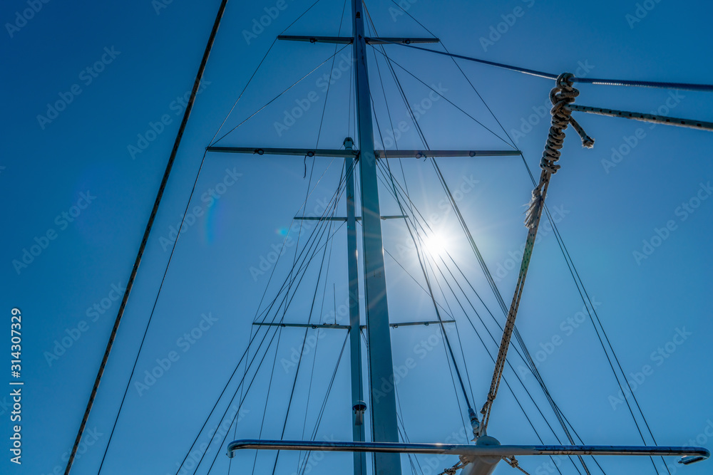 Naklejka premium Mast of the yacht against the blue sky with sun glare. Summer recreation concept. High detailed photo