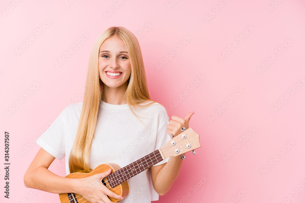 Fototapeta premium Young blonde girl playing ukelele smiling and raising thumb up