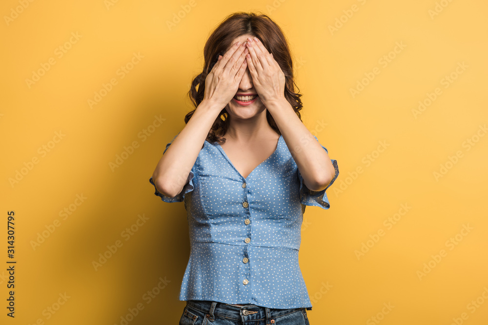 cheerful girl covering eyes with hands on yellow background cheerful girl covering eyes with hands on yellow background