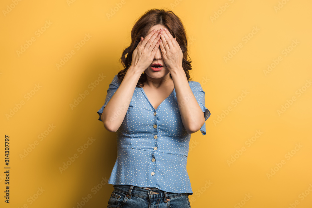shocked girl covering eyes with hands on yellow background shocked girl covering eyes with hands on yellow background