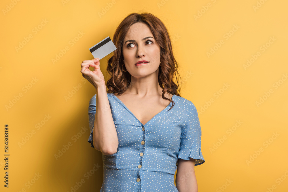 dreamy young woman holding credit card on yellow background dreamy young woman holding credit card on yellow background