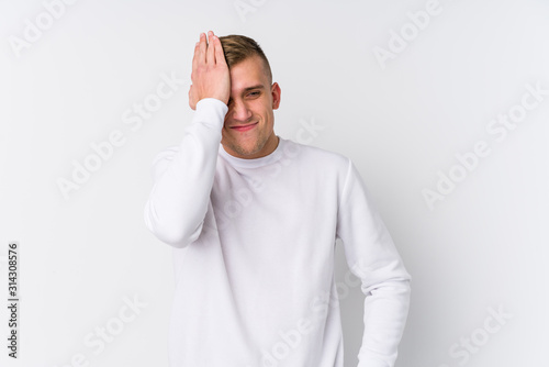 Young caucasian man on white background forgetting something, slapping forehead with palm and closing eyes.