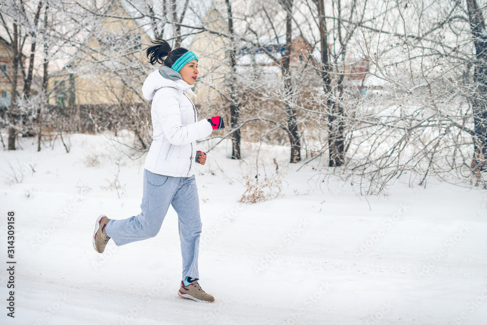 Running sport woman. Female runner jogging in cold winter forest wearing warm sporty running clothing and gloves
