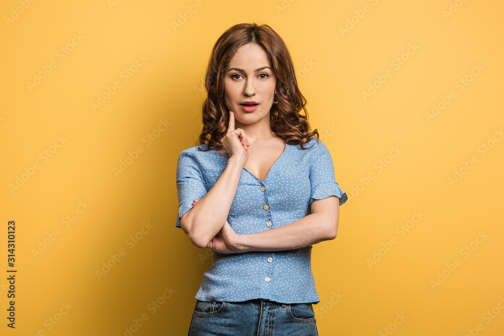 pensive girl touching face while looking at camera on yellow background pensive girl touching face while looking at camera on yellow background
