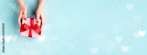 Female hands holding pink gift box tied with red bow on blue background with ...