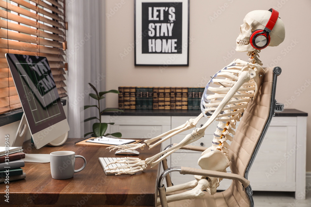 Human skeleton with headphones using computer at workplace Stock