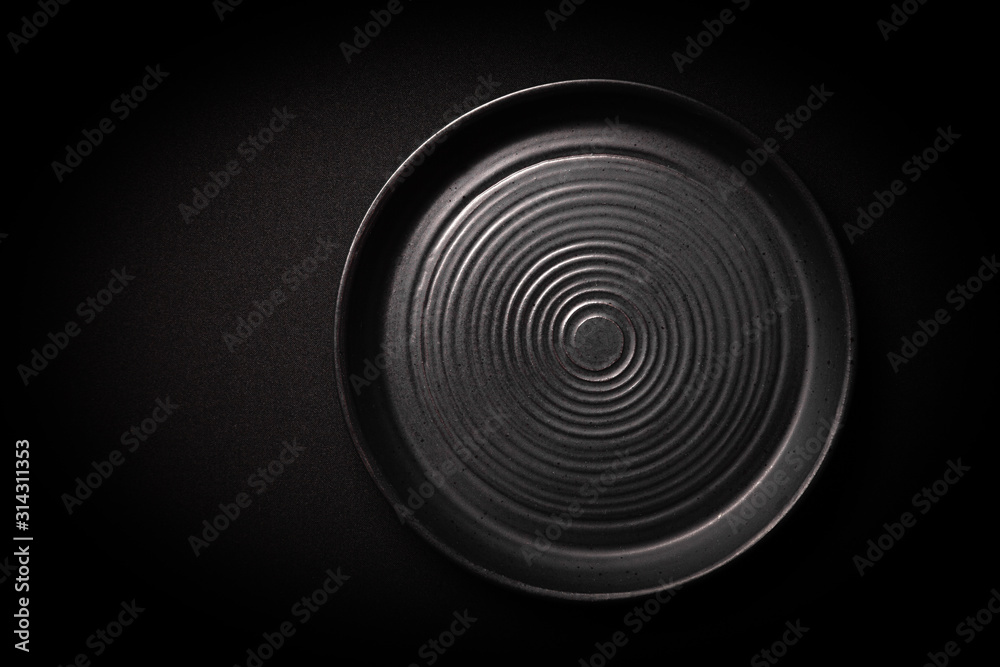 Closeup empty round black ceramic plate with pattern of circles on dark background with copy space. Overhead view. Concept modern shooting menu from chef, restaurant advert, tableware catalogs, top Closeup empty round black ceramic plate with pattern of circles on dark background with copy space. Overhead view. Concept modern shooting menu from chef, restaurant advert, tableware catalogs, top