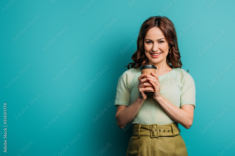cheerful girl looking at camera while holding coffee to go on blue background cheerful girl looking at camera while holding coffee to go on blue background